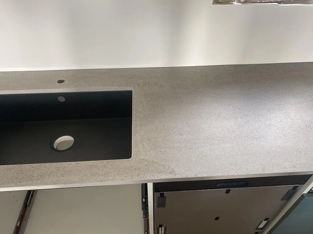 Underlimmad svart kompositdiskho i en matt grå Dekton Keon köksbänkskiva med kranhål i ett kök i Klagstorp.