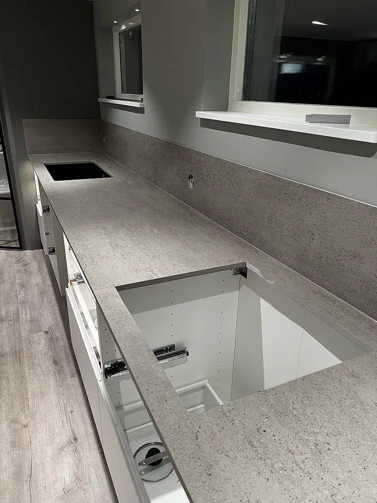 Köksbänkskiva i matt grå Dekton Keon i ett kök i Kungsbacka, med uppvikt väggbeklädnad i samma sten, underlimmad diskho och fönsterbänk, fotograferat under montering.