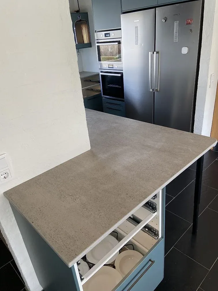 Köksö i Dekton Keon med matt betonglook och utdragen låda, framför rostfri amerikansk kyl och inbyggnadsugn i ett kök i Malmö.