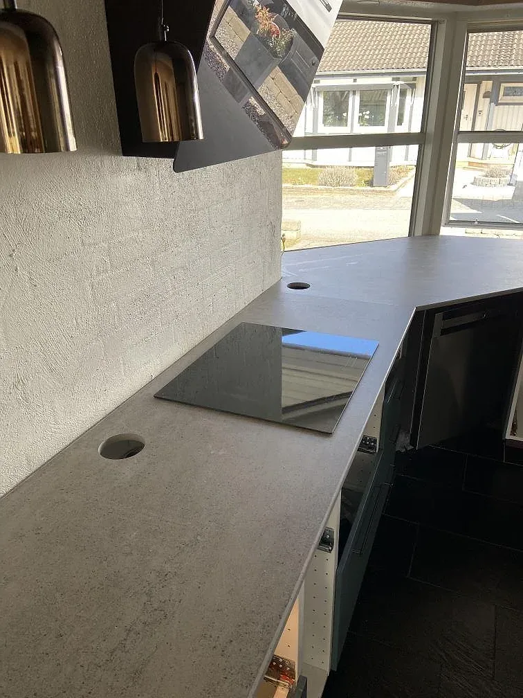 Köksbänkskiva i grå Dekton Keon med infälld induktionshäll och borrat blandarhål vid fönstret i ett kök i Malmö.