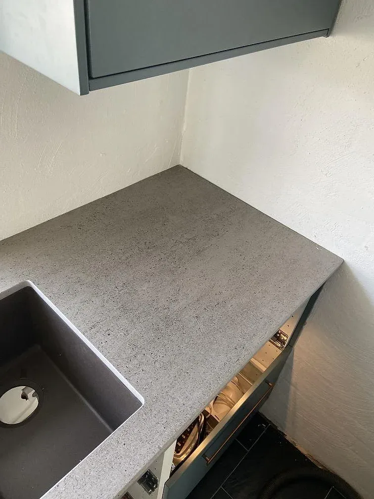 Hörn av köksbänkskiva i grå Dekton Keon med underlimmad kompositdiskho och blågröna luckor i ett kök i Malmö.
