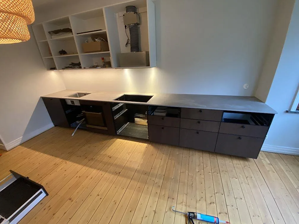Köksbänkskiva i grå Dekton Keon med matt betonglook, lång sammanhängande bänk med urtag för diskho och häll i ett kök under montering i Malmö.