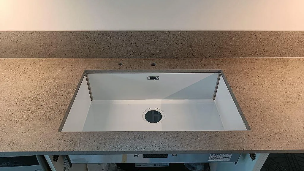 Närbild på vit underlimmad diskho i matt Dekton Keon bänkskiva med uppvikt stänkskydd i ett kök i Östra Karup.