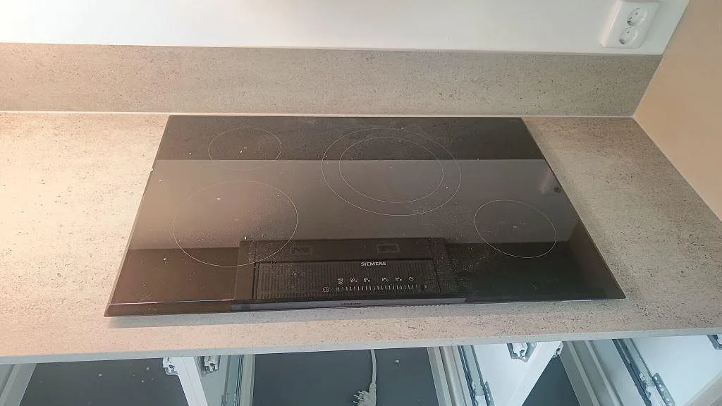 Svart induktionshäll monterad i matt Dekton Keon köksbänkskiva med grått stänkskydd i Östra Karup.