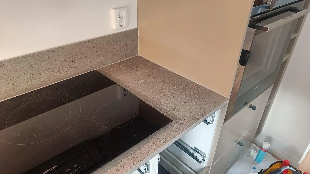 Hällsida med matt Dekton Keon bänkskiva, inbyggnadsugn och stänkskydd i ett kök under montering i Östra Karup.
