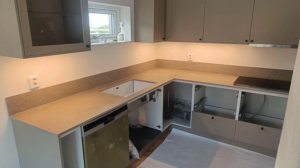 U-format kök med matt köksbänkskiva i Dekton Keon, vit underlimmad diskho, svart induktionshäll och stänkskydd i Östra Karup.