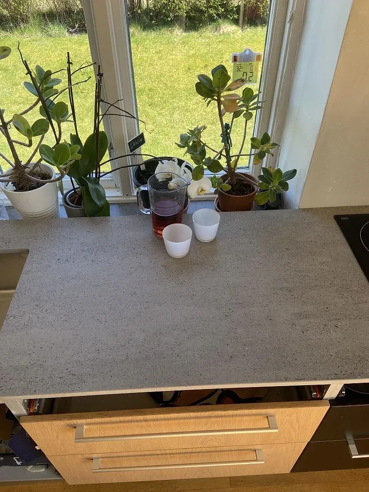 Lång köksö i grå betongliknande Dekton Keon under montering i ett kök i Rinkaby, med träklädd vägg och montörer på plats.