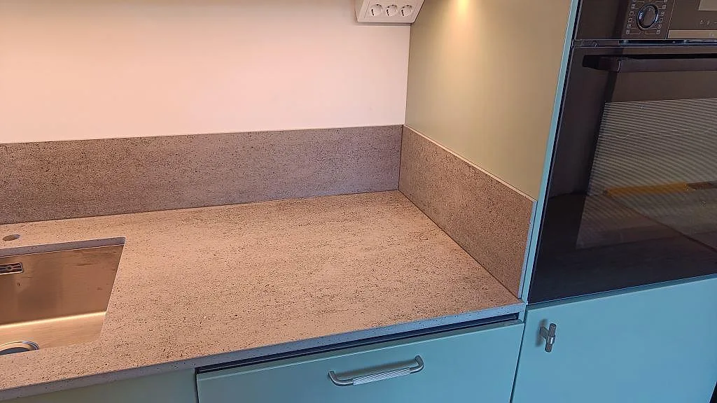 Närbild av köksbänkskiva i matt Dekton Keon, keramik, med uppvikt stänkskydd, diskho och ugnstorn i Sävedalen.