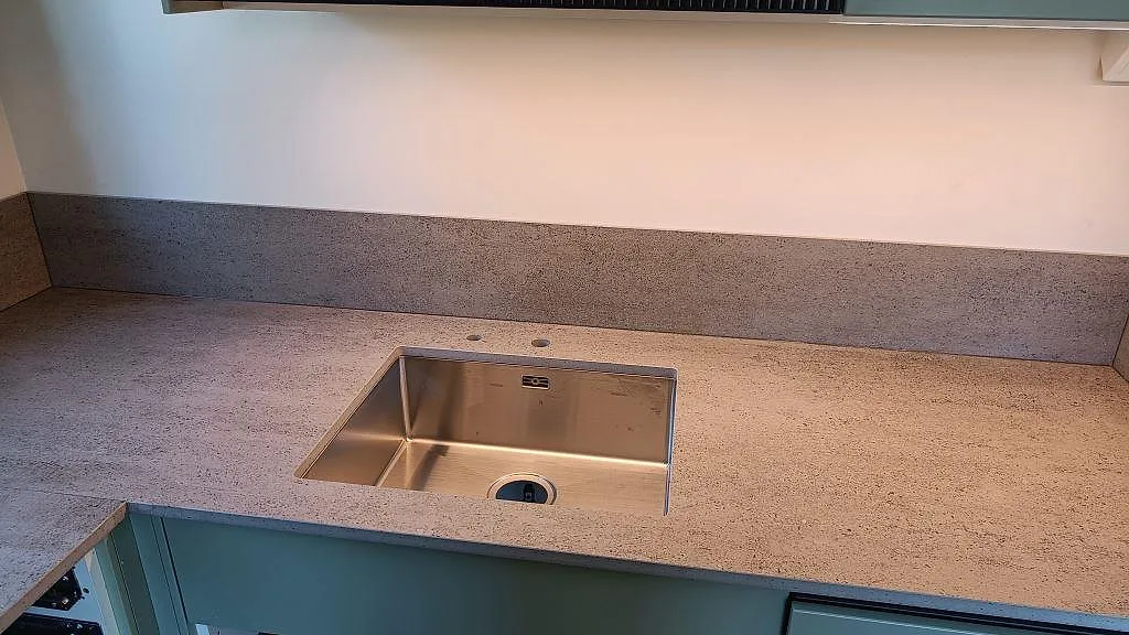 Köksbänkskiva i matt Dekton Keon, keramik, med rostfri diskho och grå stänkkant i ett kök i Sävedalen.