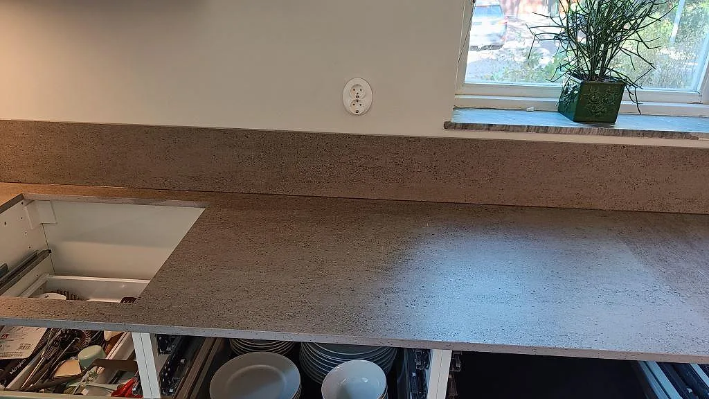Installerad köksbänkskiva i matt Dekton Keon, keramik, med grå stänkskyddsskiva och öppna köksstommar i Sävedalen.