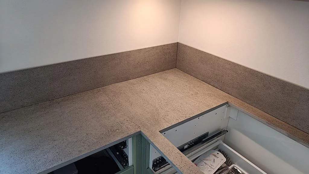 Hörnparti med köksbänkskiva i matt Dekton Keon, keramik, och matchande stänkskydd över gröna köksstommar i Sävedalen.