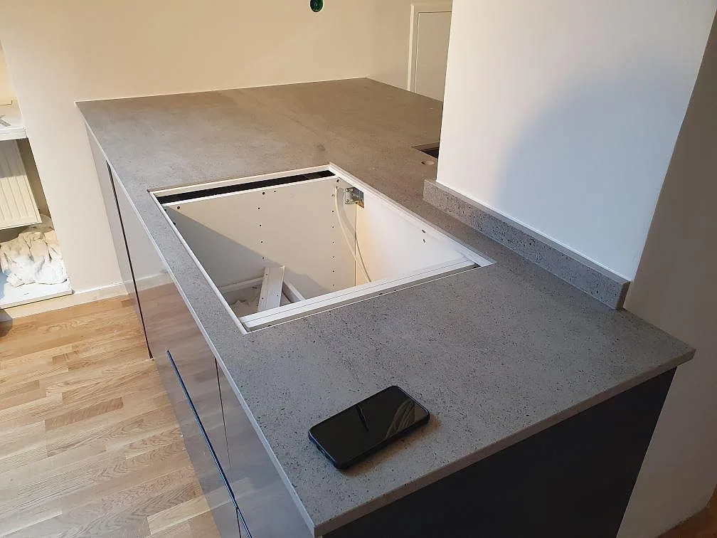 Vinklad köksbänkskiva i grå Dekton Keon, matt, med håltagning för häll, fotograferad under montering i ett kök i Stockholm.