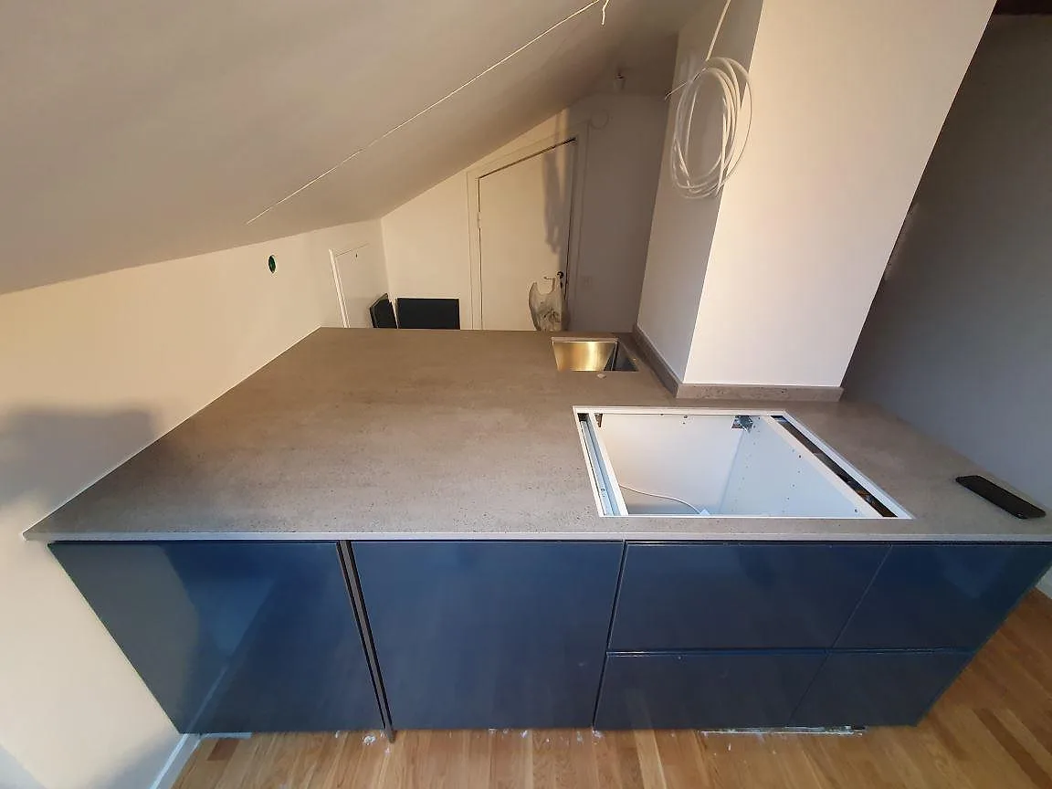 Köksdel i grå Dekton Keon med matt yta över blå högblanka luckor och en liten rostfri diskho i ett kök i Stockholm.