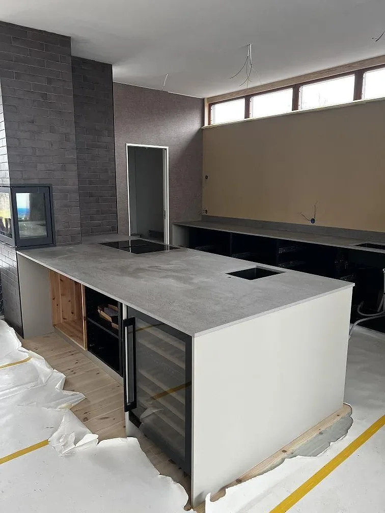 Köksö med waterfall-gavel i grå Dekton Keon, matt yta, i ett ljust kök under montering i Stora Höga.