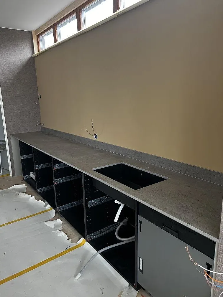 Köksö i grå Dekton Keon med urtag för häll och underlimmad diskho ovanpå öppna stommar under montering i Stora Höga.