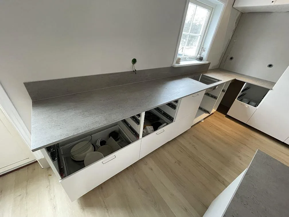 Matt köksbänkskiva i Dekton Keon längs väggen med fönsterbänk och öppna lådstommar i ett kök i Surahammar.