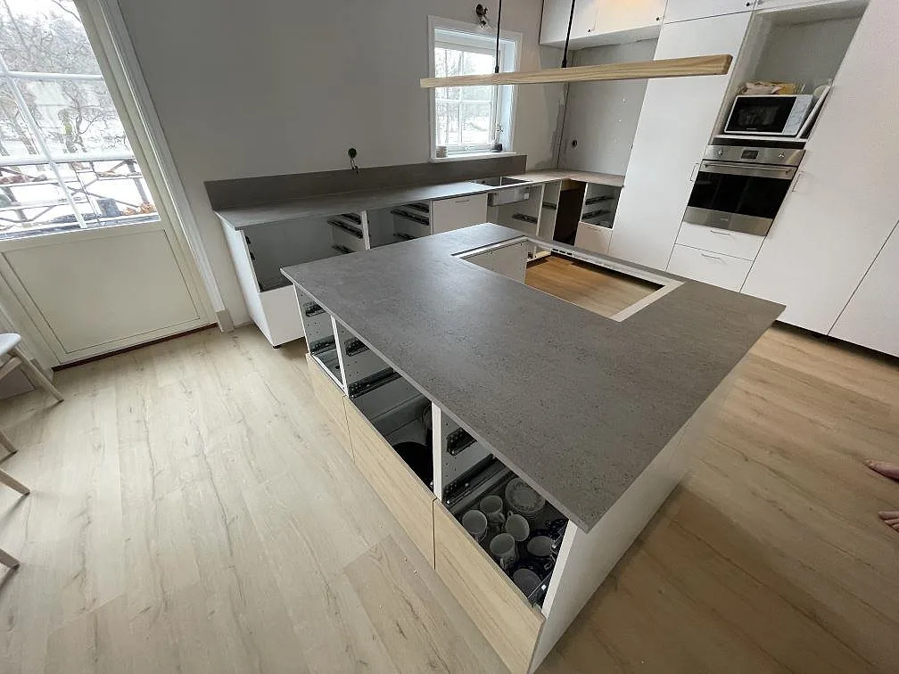 Köksbänkskiva och köksö i grå Dekton Keon, matt, med urtag för häll i ett kök under montering i Surahammar.