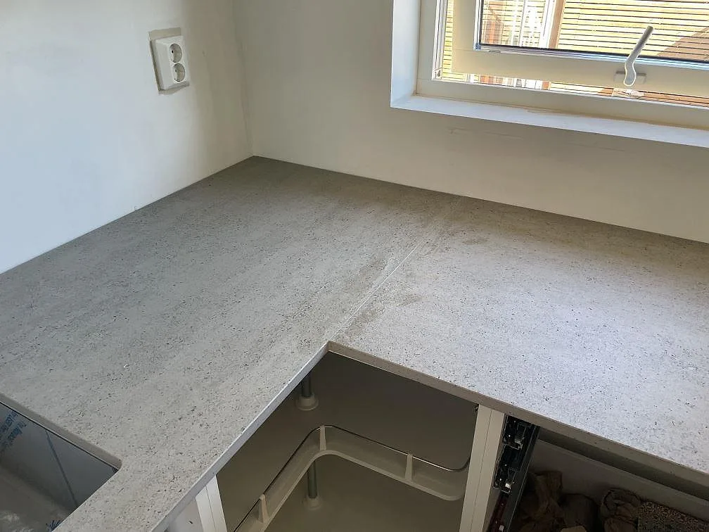 L-formad köksbänkskiva i Dekton Keon keramik, matt, med diskho och yta vid fönster i Tygelsjö.
