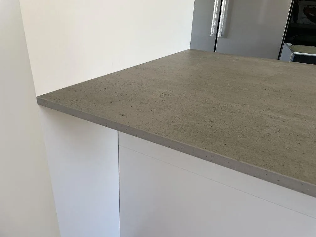 Detalj av matt Dekton Keon keramik som köksbänkskiva med grå kantprofil och vit köksinredning i Tygelsjö.