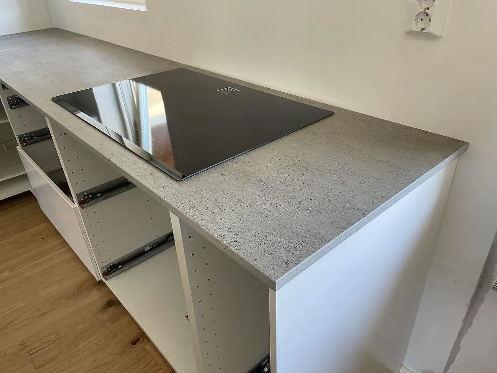 Köksbänkskiva i Dekton Keon keramik, matt, med svart induktionshäll och vita köksstommar i Tygelsjö.