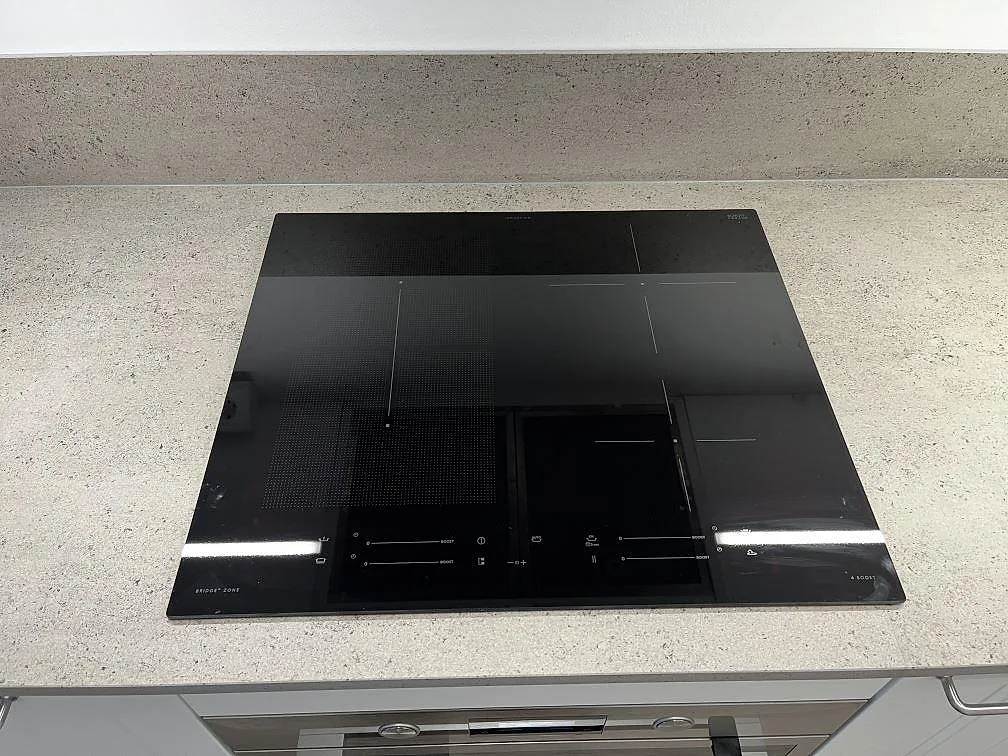 Närbild på svart induktionshäll infälld i matt Dekton Keon, keramik, med matchande stänkskydd i kök i Västerås.