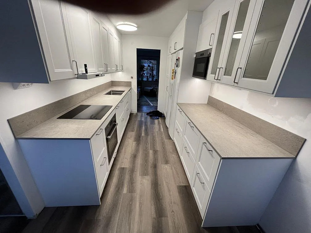 Köksbänkskivor i matt Dekton Keon, keramik, med svart induktionshäll, rostfri diskho och stänkskydd i ett galleykök i Västerås.