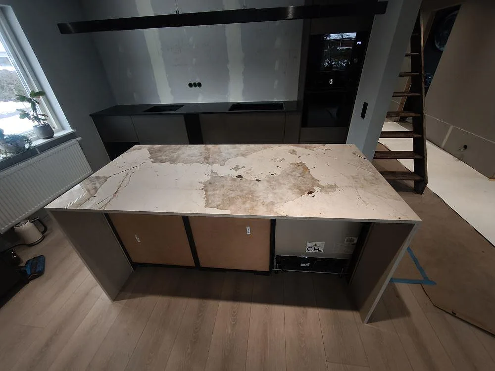Polerad Dekton Khalo på köksö med breda grå och varma ådringar under montering i Bjuv.