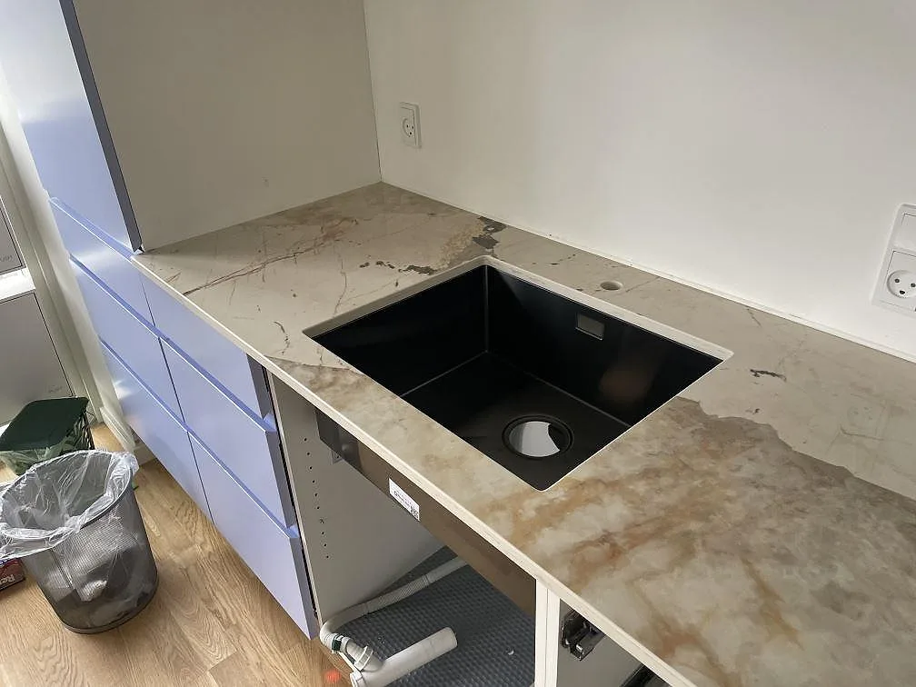 Polerad Dekton Khalo keramik med underlimmad svart diskho och beigegrå ådring under montering i København.