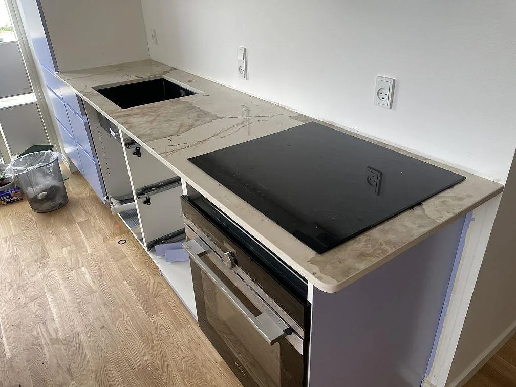 L-formad köksbänkskiva i polerad Dekton Khalo keramik med svart häll och underlimmad svart diskho i ett kök i København.