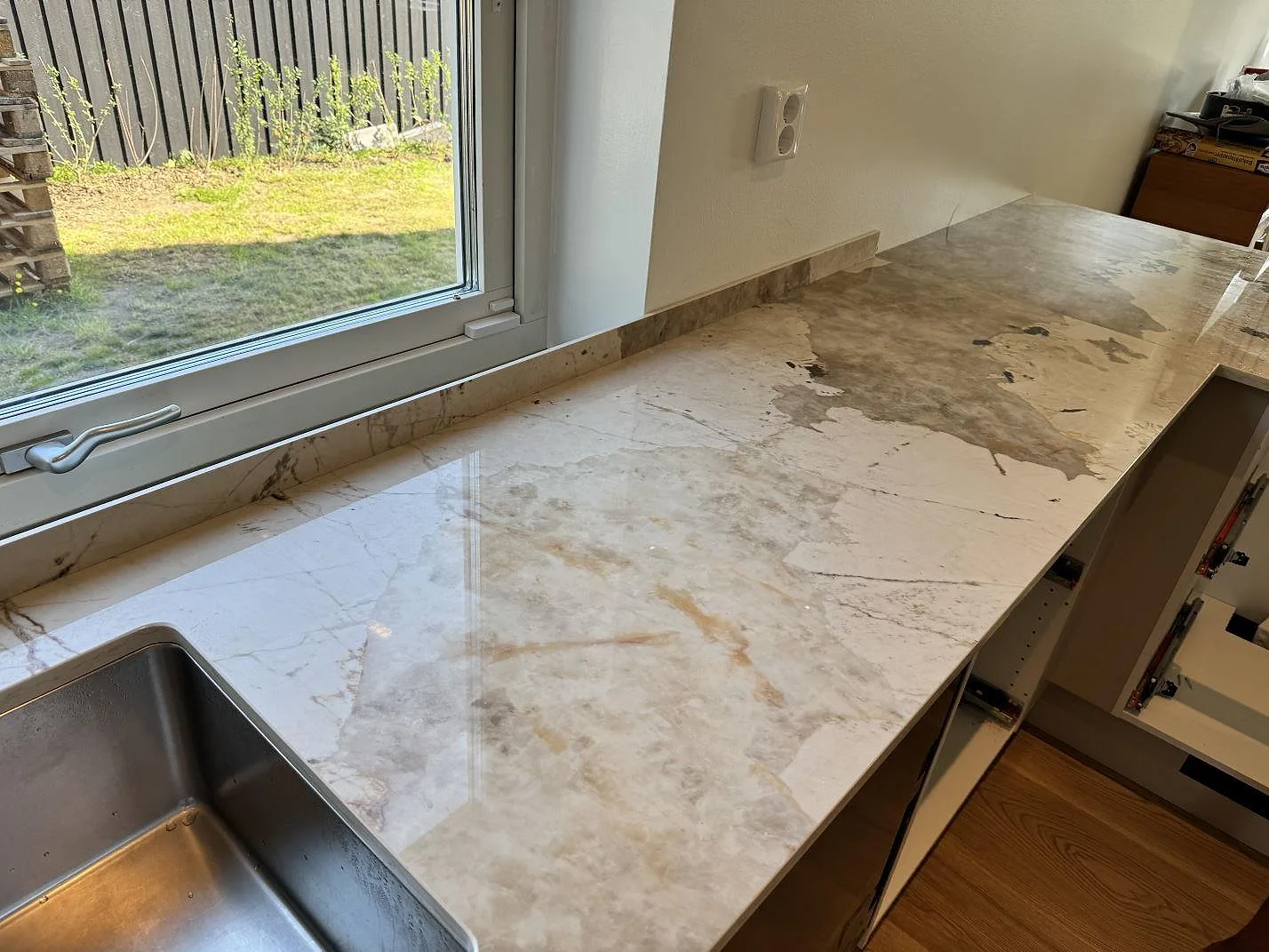 Lång polerad bänkskiva i Dekton Khalo vid fönster, med diskho i ena kanten och låg stänkkant i Malmö.