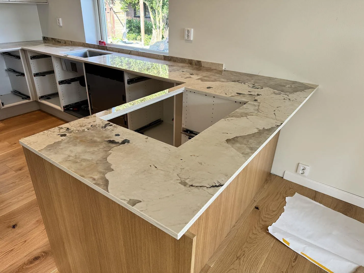 Polerad köksbänkskiva i Dekton Khalo med halvö, låg stänkkant och öppna köksstommar under montering i Malmö.