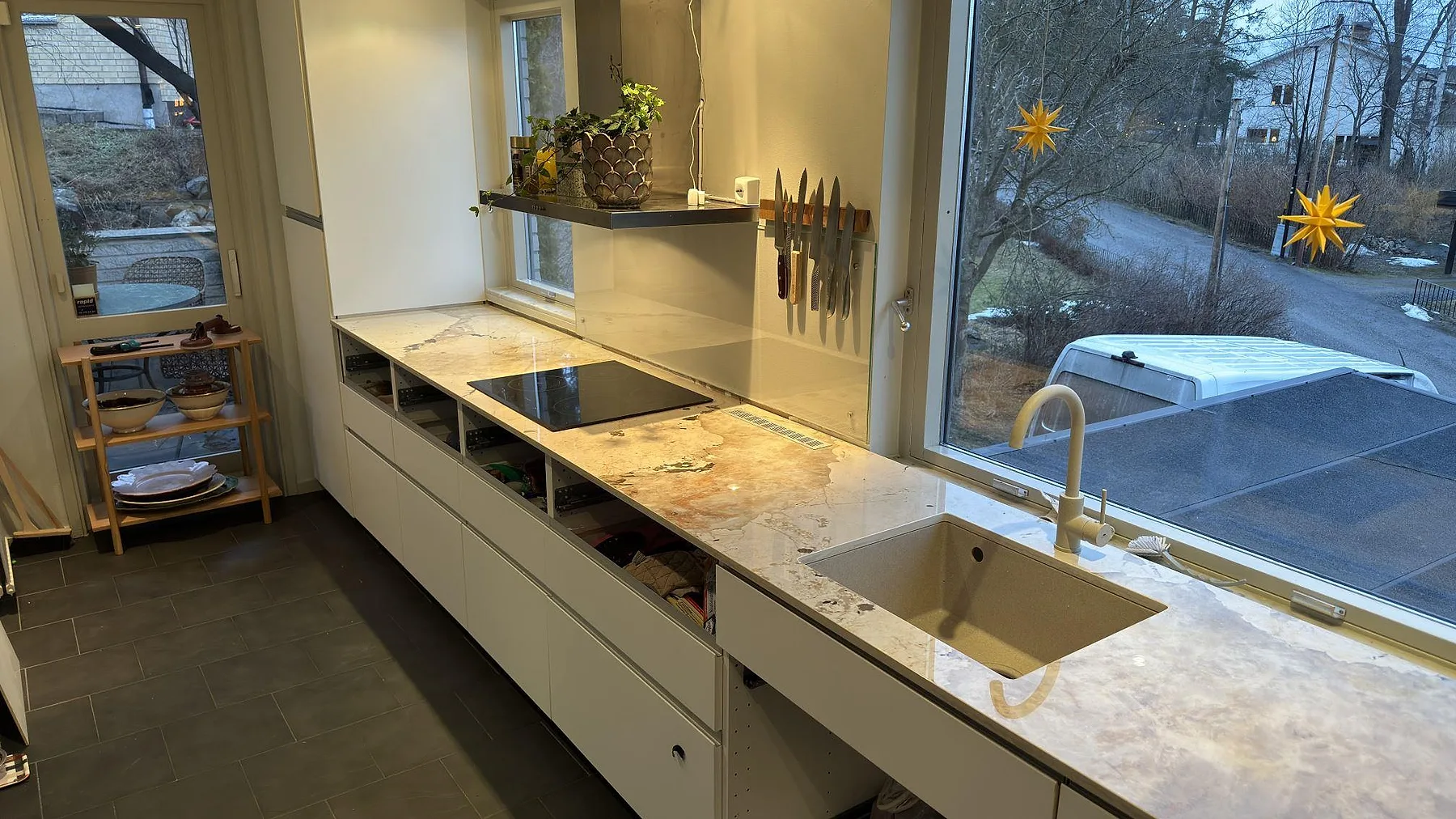 Bänkrad i Dekton Khalo längs fönstret i ett kök i Nacka med underlimmad sandfärgad diskho, mässingsblandare och induktionshäll bredvid.