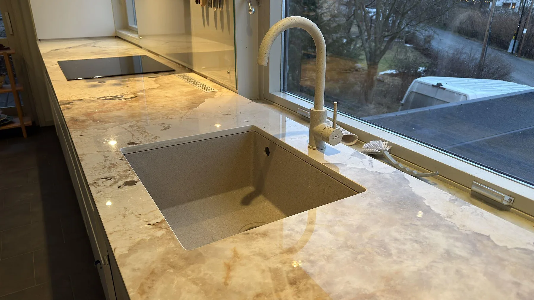 Detalj av underlimmad diskho i Dekton Khalo med mässingsblandare och induktionshäll i ett kök i Nacka, polerad keramik med ljus ådring.