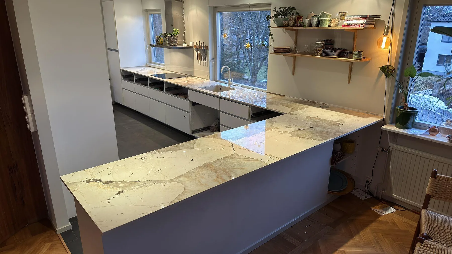 Köksbänkskiva i ljus Dekton Khalo, polerad keramik med gyllen och grå ådring, i ett kök i Nacka med halvö och bänkrad längs fönstret, fotat under montering.