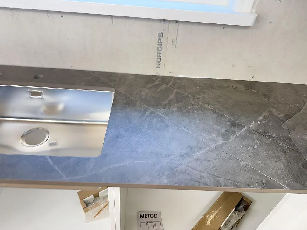 Grå Dekton Kira bänkskiva i matt finish sedd uppifrån med rostfri diskinsats vid fönstret i ett kök i Immeln.