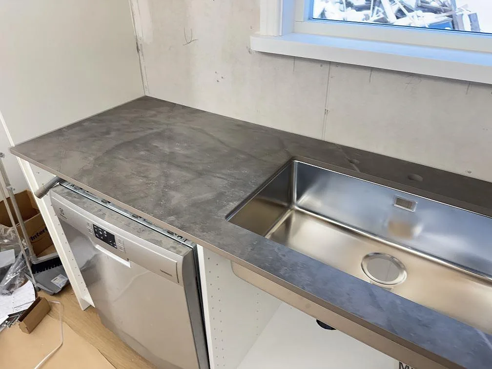 Köksbänkskiva i grå Dekton Kira med stor underlimmad rostfri diskho och inbyggd diskmaskin i ett kök i Immeln.