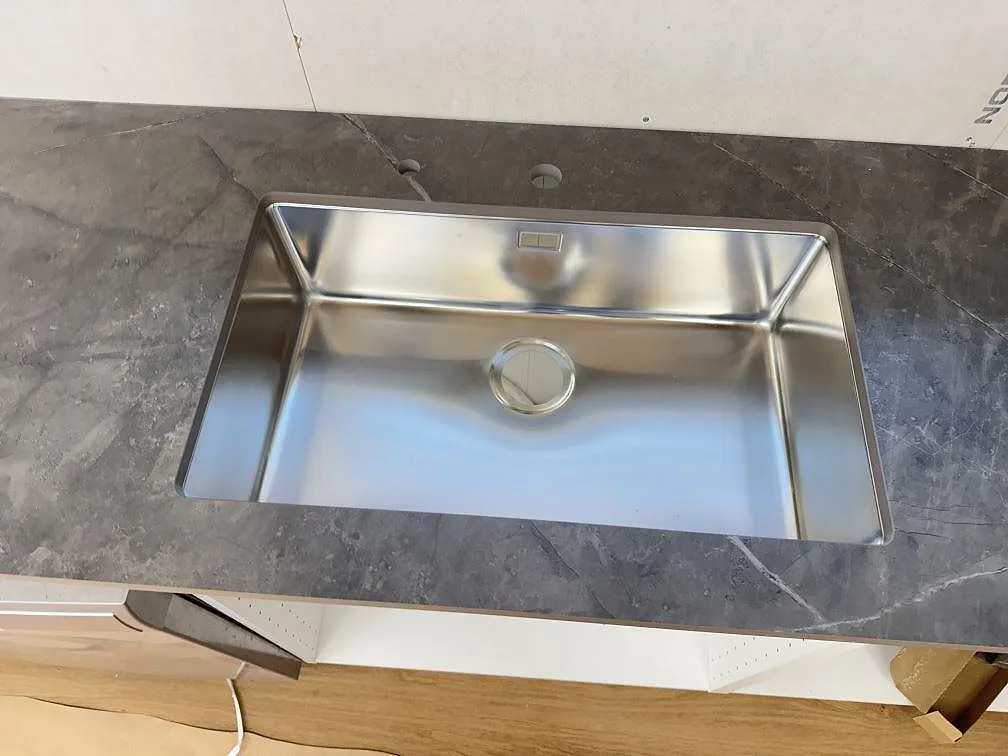Stor underlimmad rostfri diskho monterad under grå Dekton Kira bänkskiva med tydlig ådring i ett kök i Immeln.