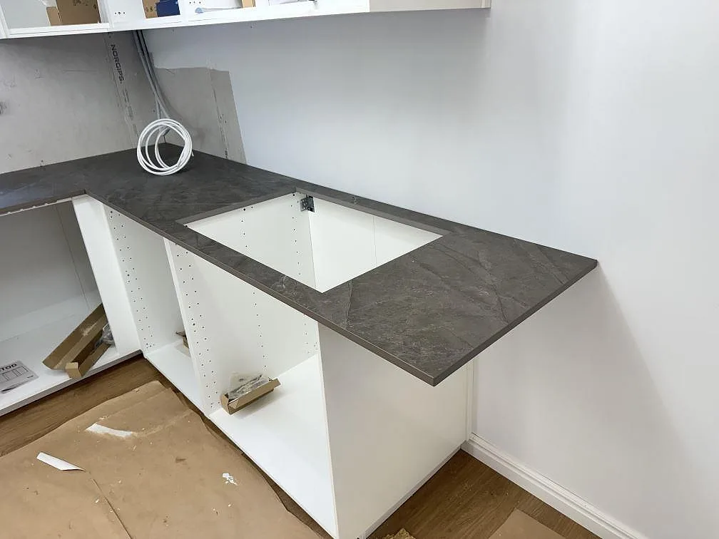 Köksbänkskiva i grå Dekton Kira, matt, L-format bänkparti med urtag för diskho i ett kök under montering i Immeln.