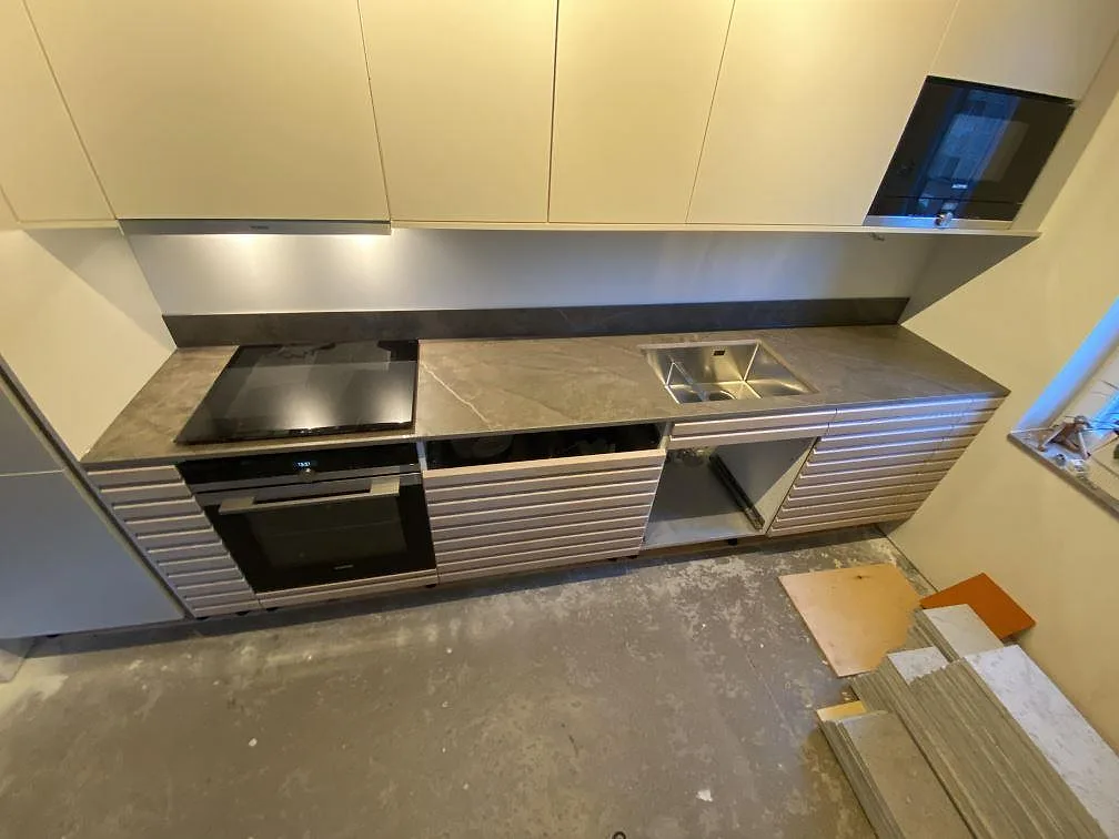 Matt köksbänkskiva i grå Dekton Kira med svart häll, rostfri diskho och stänkskydd i ett kök i Kungsbacka.