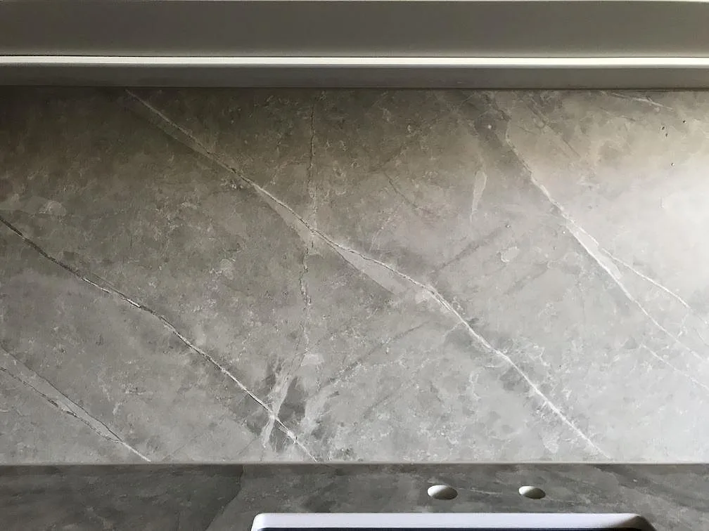 Stänkskydd i matt grå Dekton Kira med tydlig ådring ovanför bänkskivan med förborrade blandarhål i ett kök i Malmö.