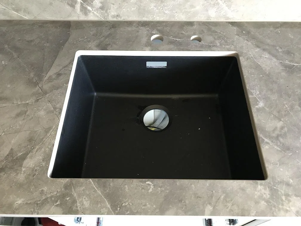 Underlimmad svart komposithoar infälld i en bänkskiva av matt grå Dekton Kira med två förborrade blandarhål i ett kök i Malmö.