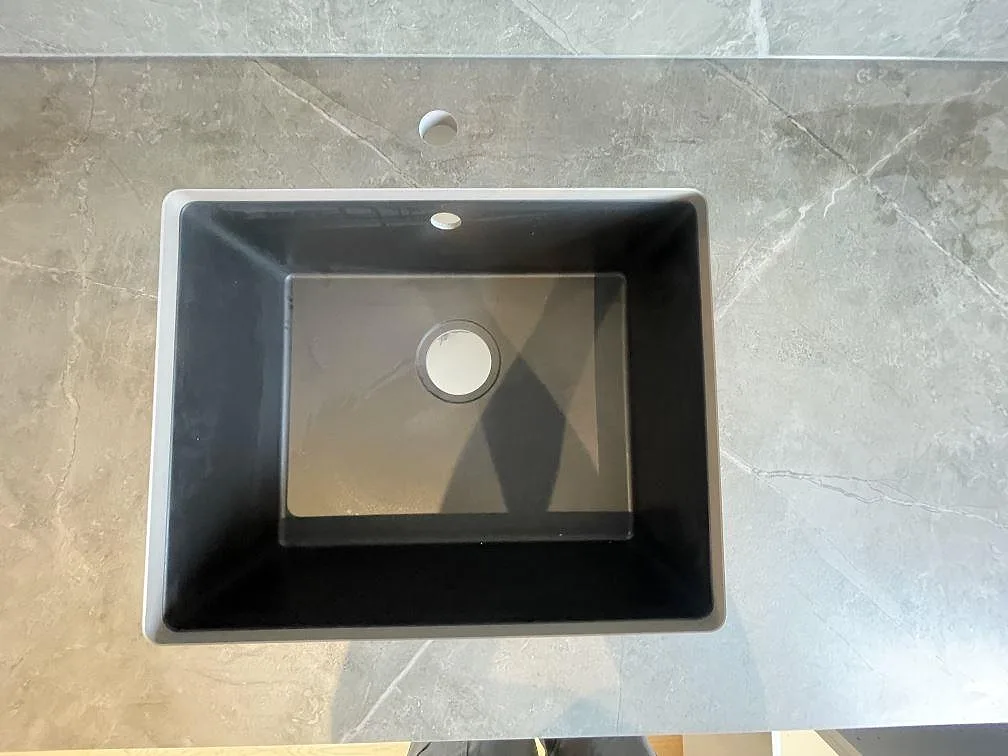 Underlimmad svart kompositdiskho sedd ovanifrån, infälld under en matt köksbänkskiva i grå Dekton Kira i Strängnäs.