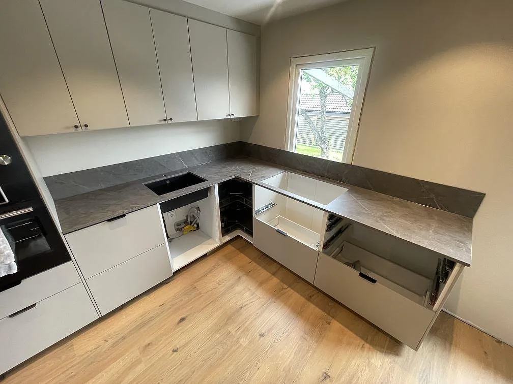 Köksbänkskiva i grå Dekton Kira, matt, med underlimmad svart kompositdiskho och matchande stänkskydd i ett vinkelkök under montering i Strängnäs.