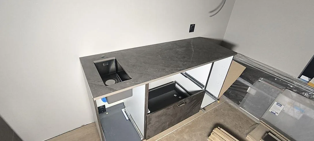 Köksbänkskiva i grå Dekton Kira, matt keramik, med underlimmad diskho mot vit vägg i ett kök under montering i Uppsala.