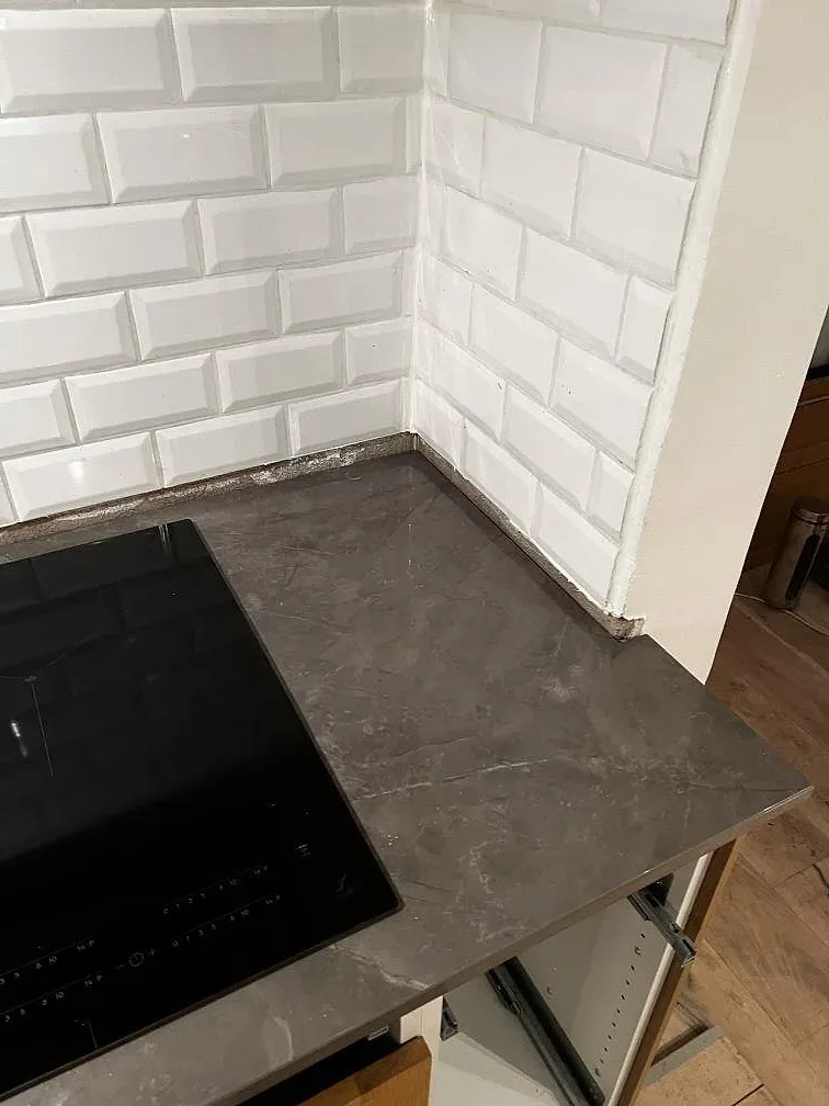 Hörndetalj av polerad Dekton Korso runt svart induktionshäll och vit kakelvägg i kök i Arlöv.
