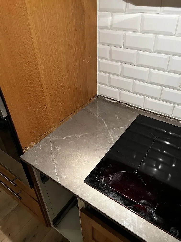 Polerad Dekton Korso i kökshörn med svart häll, vit kakelvägg och träinredning i Arlöv.