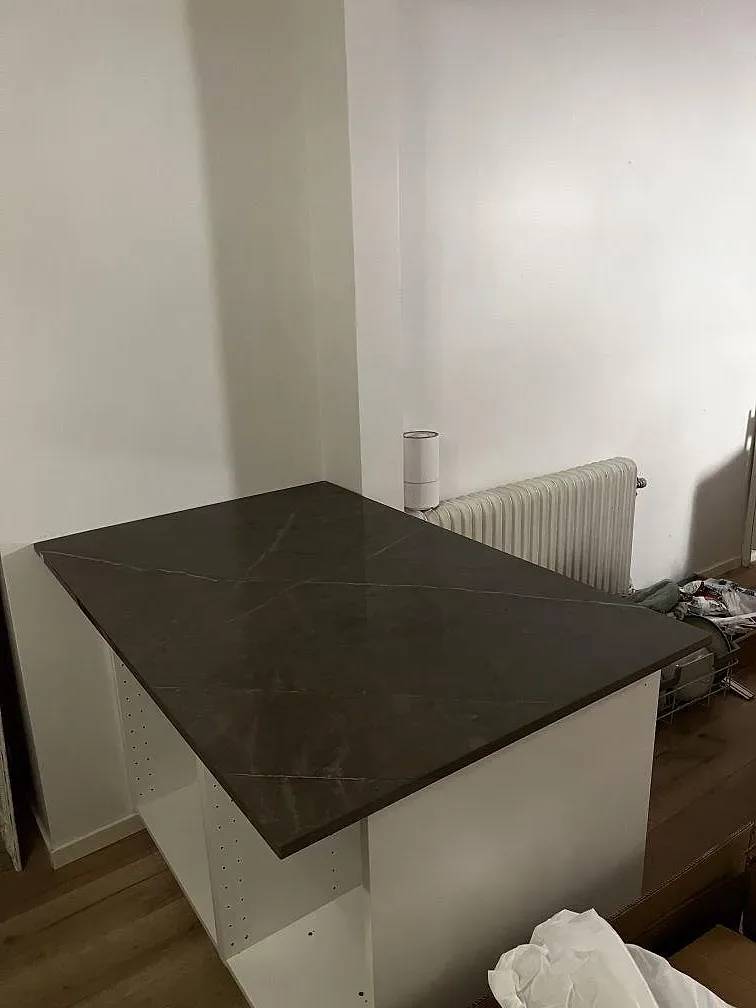 Sidovy av installerad köksbänkskiva i polerad Dekton Korso på vita stommar under montering i Arlöv.