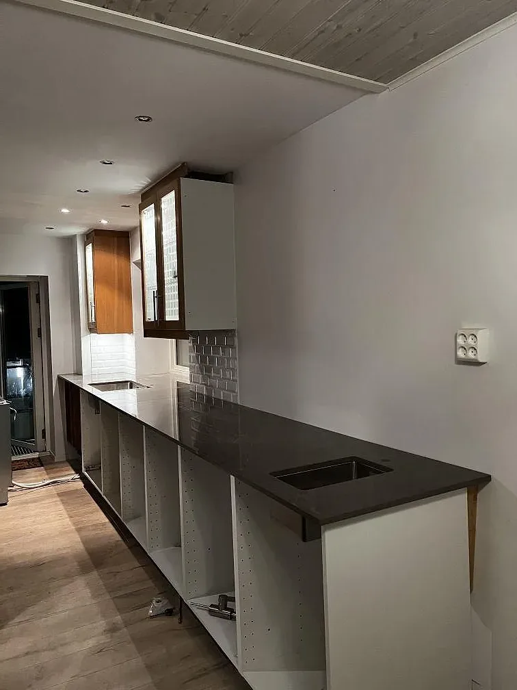 Lång köksbänk i polerad Dekton Korso med underlimmad rostfri diskho och vita köksstommar under montering i Arlöv.