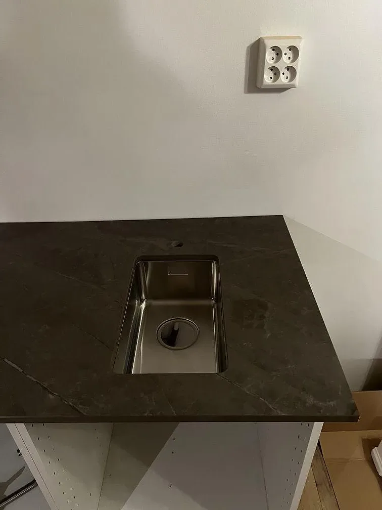 Närbild på underlimmad rostfri diskho i polerad Dekton Korso, grå keramikbänkskiva i kök i Arlöv.