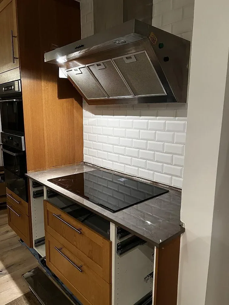 Köksbänkskiva i grå Dekton Korso, polerad keramik, med svart induktionshäll och vit kakelvägg i ett kök i Arlöv.